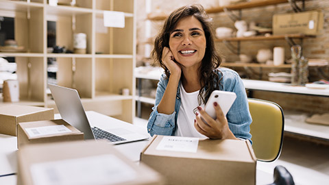 Cheerful online store owner looking away thoughtfully while holding a smartphone