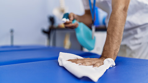 man wearing physiotherapist uniform disinfecting massage table at rehab clinic