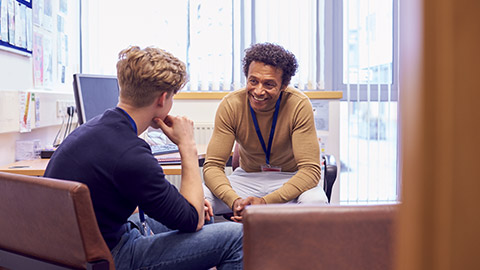 Male College Student Meeting With Campus Counselor Discussing Mental Health Issues