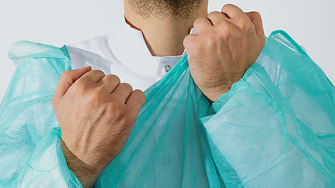 A man wearing a green surgical apron and a face mask