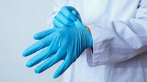 doctor man, wearing a white coat, putting on a pair of blue surgical gloves