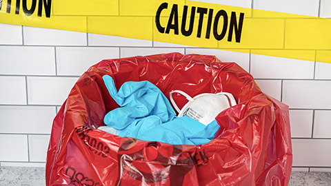 biohazard trash bag with used N95 respirator mask, medical exam gloves and caution tape