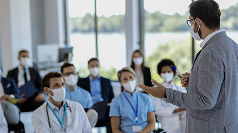 Male holding a training class to large group of healthcare workers and business people