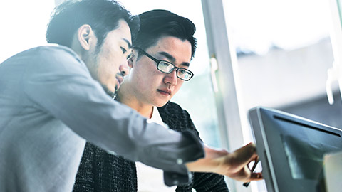 A man training a colleague, pointing to a computer screen