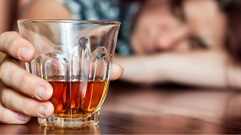 Drunk woman holding an alcoholic drink and sleeping with her head on the table