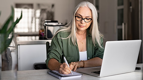 woman taking notes in notebook while using laptop at home