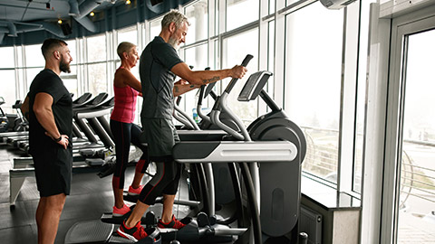 Couple of attractive and fit retire woman and man excercising on stepper at gym under trainers supervision