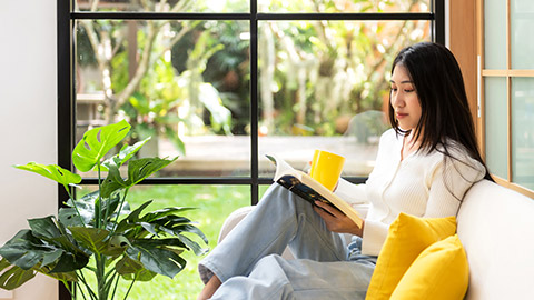 Happy young woman reading book on sofa at home