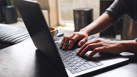 Closeup image of a woman working and typing on laptop computer keyboard on wooden table