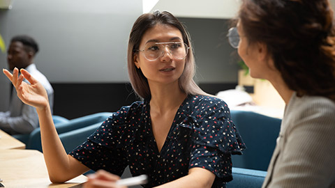 Asian businesswoman wearing glasses sharing ideas, brainstorming, discussing project with colleague at workplace