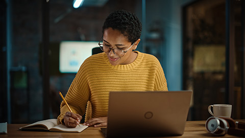 Young Hispanic Marketing Specialist Working on Laptop Computer in Busy Creative Office Environment