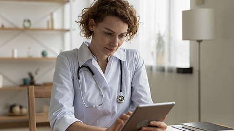 doctor wearing white coat and stethoscope holding a tablet