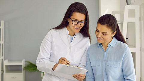 Friendly nurse holding clipboard and communicating with patient