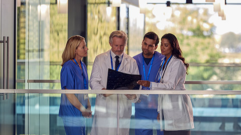 Medical Team Wearing White Coats and Scrubs Discuss Patient Scan Meeting in Hospital