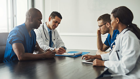 medical team having a meeting with doctors in white lab coats and surgical scrubs seated at a table