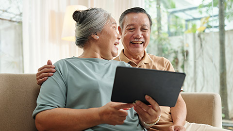 Joyful senior couple watching funny videos on tablet computer