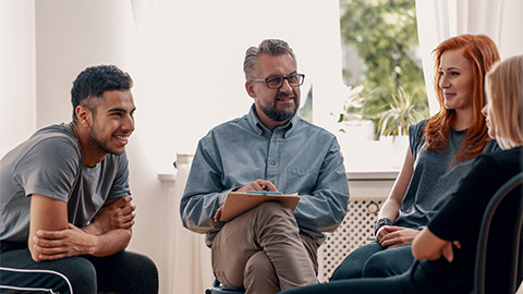 Smiling spanish man talking to his friends during meeting for teenagers with therapist