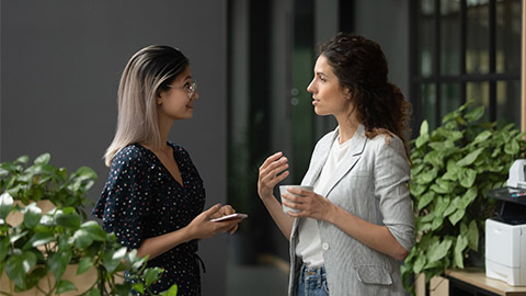 Asian and Caucasian ethnicity businesswoman talking discuss common project standing in workplace hall