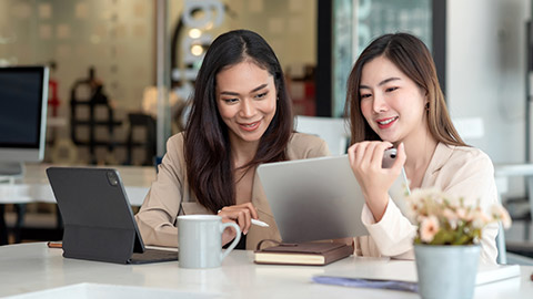 Two young Asian woman discuss concept work at the office using a tablet.