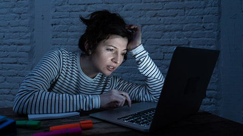 Overworked and tired female student working late at night on laptop trying not to fall asleep