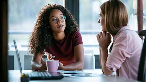 Shot of two beautiful business women working together with laptop while talking about job news in the office.