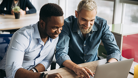 Company employees work at a laptop in their office developing new successful ideas for their company