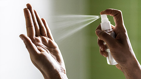 A close up image of a person spraying disinfectant on other hand hand