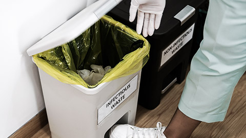 Close up of hospital worker discarding infectious medical waste into disposal container bin