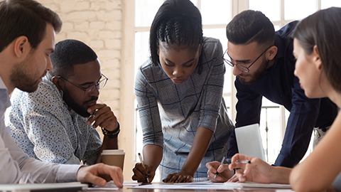 millennial female team leader leaned over table, writing down project ideas