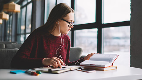 Attractive hipster girl learning at university library while enjoying favourite music