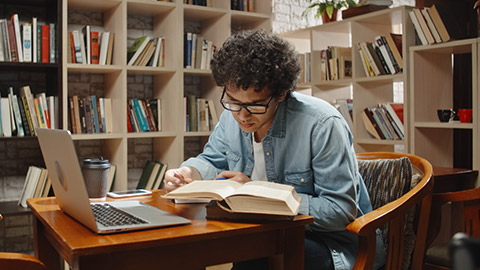 Asian student doing research in library using laptop in books