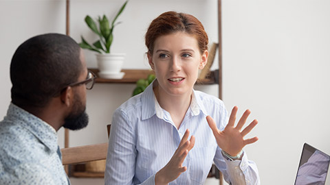 Two diverse businesspeople chatting sitting behind laptop in office