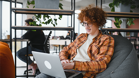 male freelancer in trendy apparel sitting at cafeteria table and doing remote work