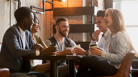 Multiracial friends having fun and laughing drinking coffee in coffeehouse