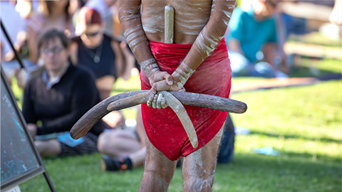 Australian Aboriginal culture, a man is holding boomerangs behind his back