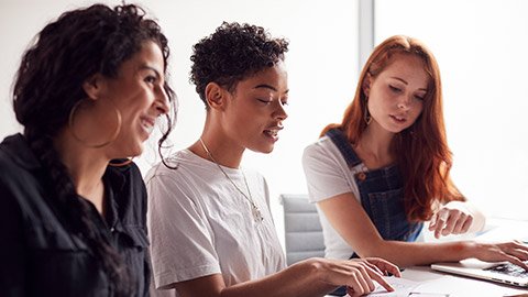 Team Of Young Businesswomen In Meeting Around Table In Modern Workspace