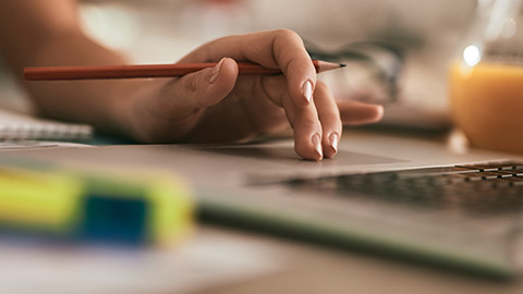 A close view of a person using a laptop while holding a pencil