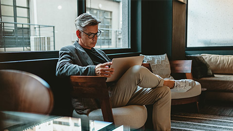 Mature businessman sitting in office lobby with a laptop