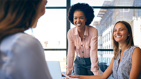 Female Multi-Cultural Business Team Meet Around Boardroom Table With Laptops Discussing Documents