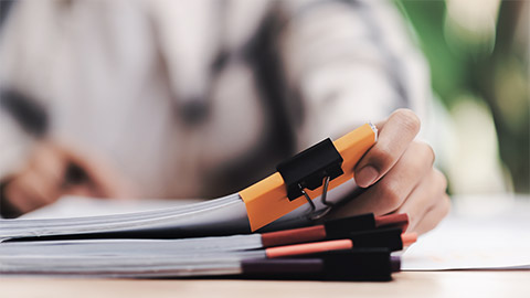 A person reading and noting a pile of paper