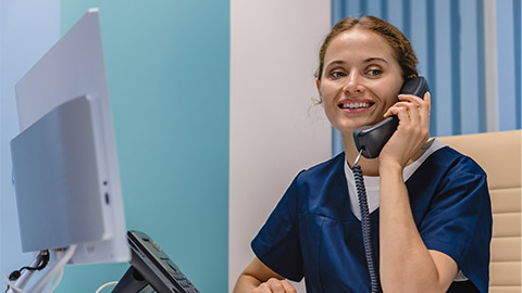 Smiling young woman nurse receptionist talking on phone while working in modern clinic.