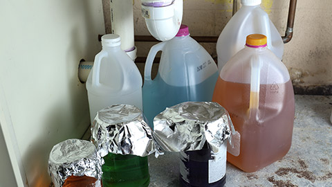 Variety in mysterious chemicals stored improperly and unlabeled in jugs and jars under a sink