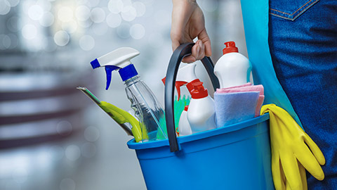 Cleaning lady holding a bucket of cleaning products in her hands on a blurred background