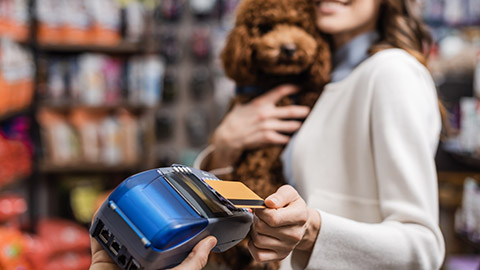 Blurred woman holding poodle and paying with credit card in pet shop