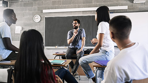 students listening and talking to friendly young male teacher