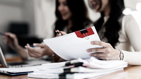 Two people using a laptop while holding paper documents