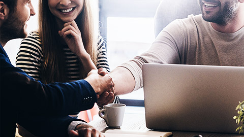 Close-up of two employees and lawyer shaking hands and smiling while sitting at the desk