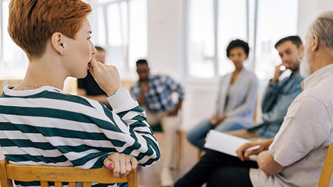 Rear view of thoughtful young woman thinking about mental problem sitting in circle during group therapy session