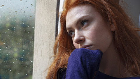 Portrait of worried girl looking through the window at home