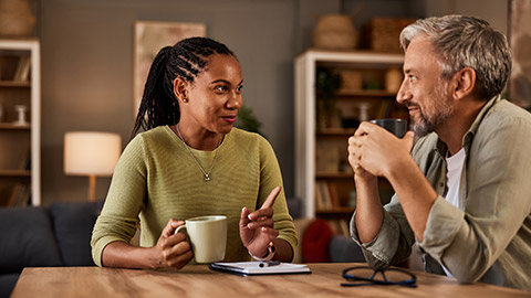 Two experienced individuals are deep in conversation while enjoying a comforting drink at their home table